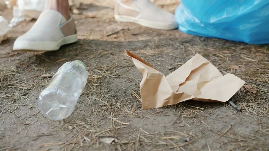 Discarded plastic bottle and paper on the ground near someone's feet.